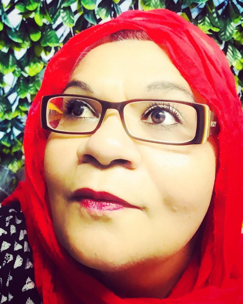 A woman with rectangular glasses and a red headscarf looks up and to the side