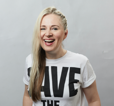 A laughing woman with long blonde hair falling over one shoulder, wearing a white t-shirt with black lettering that reads Save The Future