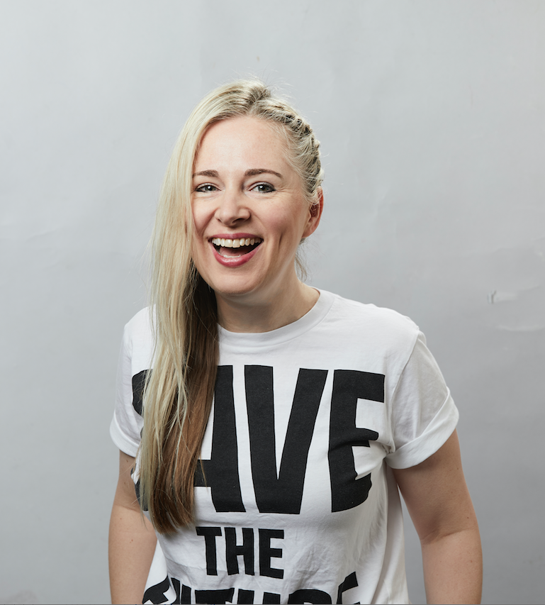 A laughing woman with long blonde hair falling over one shoulder, wearing a white t-shirt with black lettering that reads Save The Future