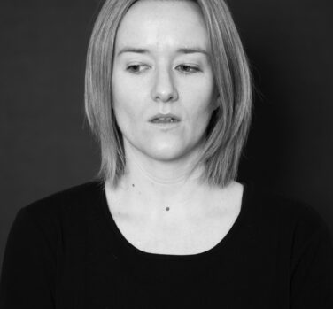 A black and white headshot of a woman with short, light hair, looking sideways