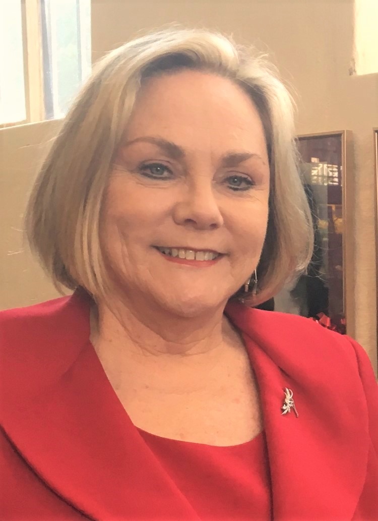 A head shot of a middle aged woman with short blonde hair and a red suit.