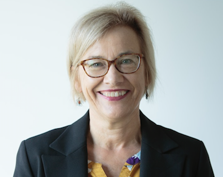 A head shot of a middle aged woman with short blonde hair and glasses, smiling widely.