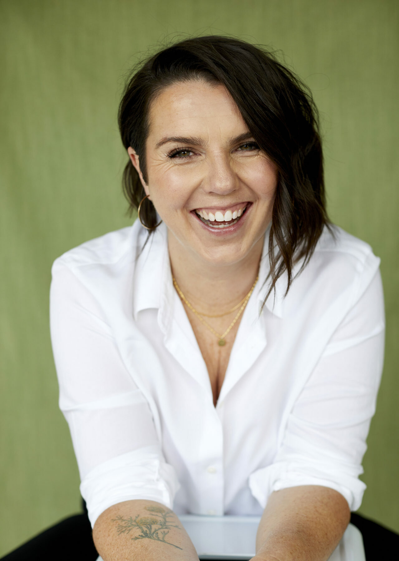 A photograph of a laughing white woman with shoulder length straight dark hair and a white blouse