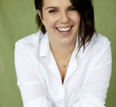 A photograph of a laughing white woman with shoulder length straight dark hair and a white blouse