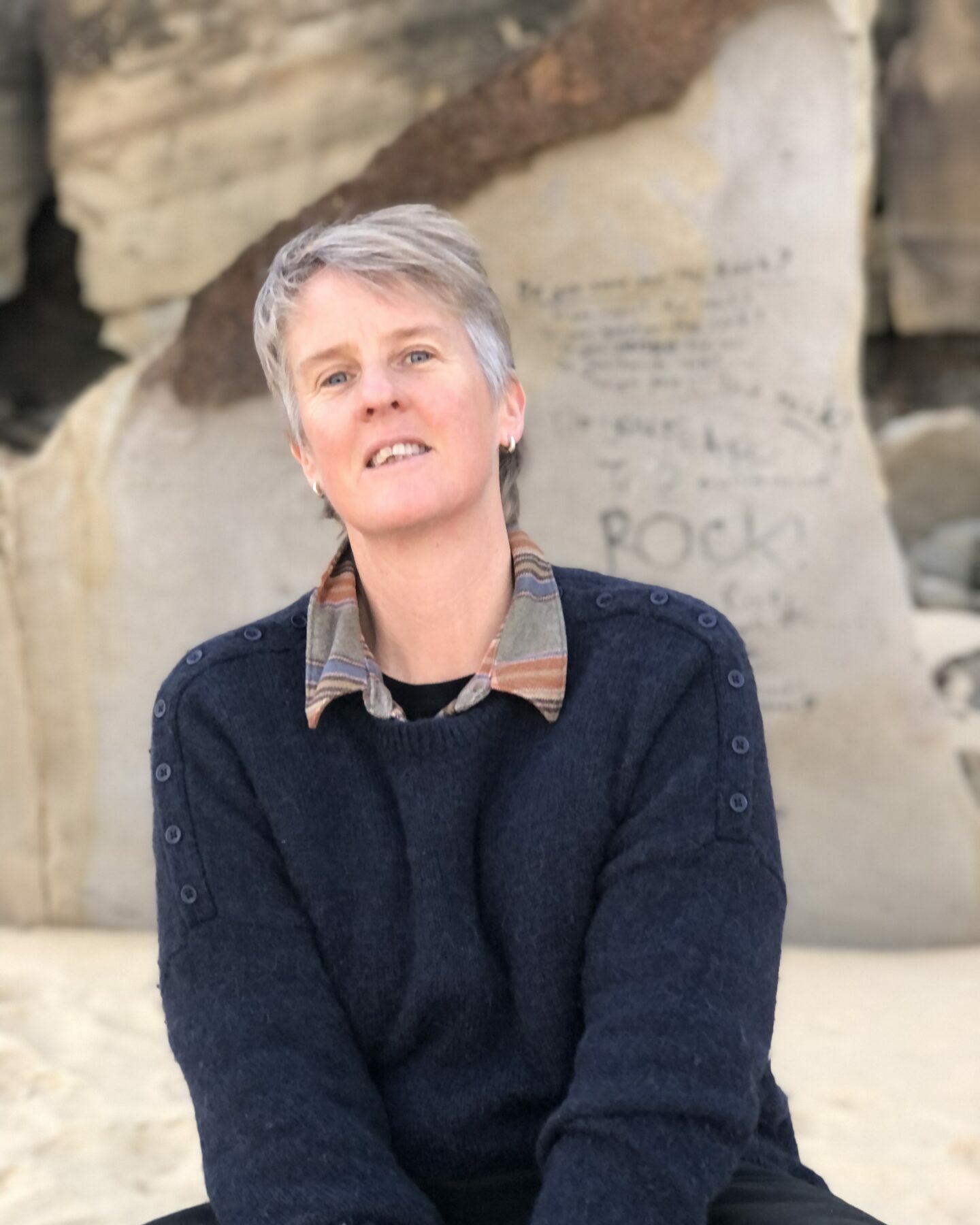 A woman with short gray hair leans away and tilts her chin up while smiling