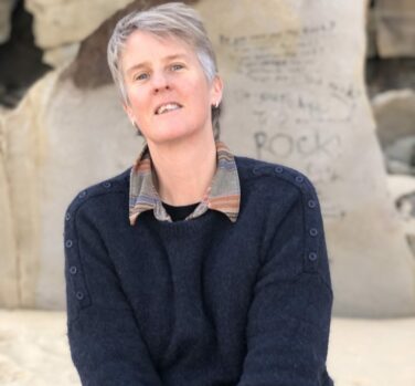 A woman with short gray hair leans away and tilts her chin up while smiling