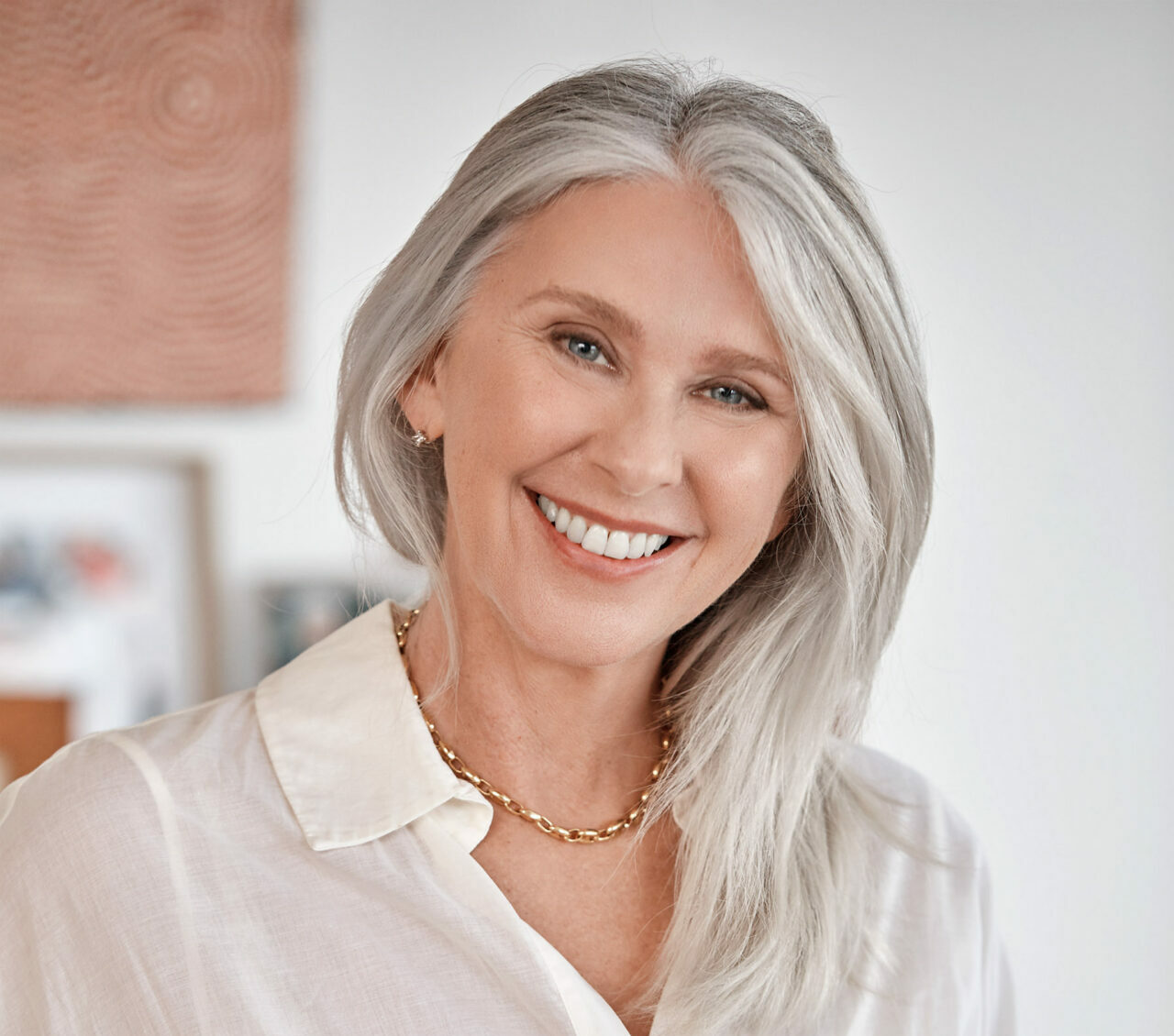 A woman with long grey hair and a button-up white dress smiles widely