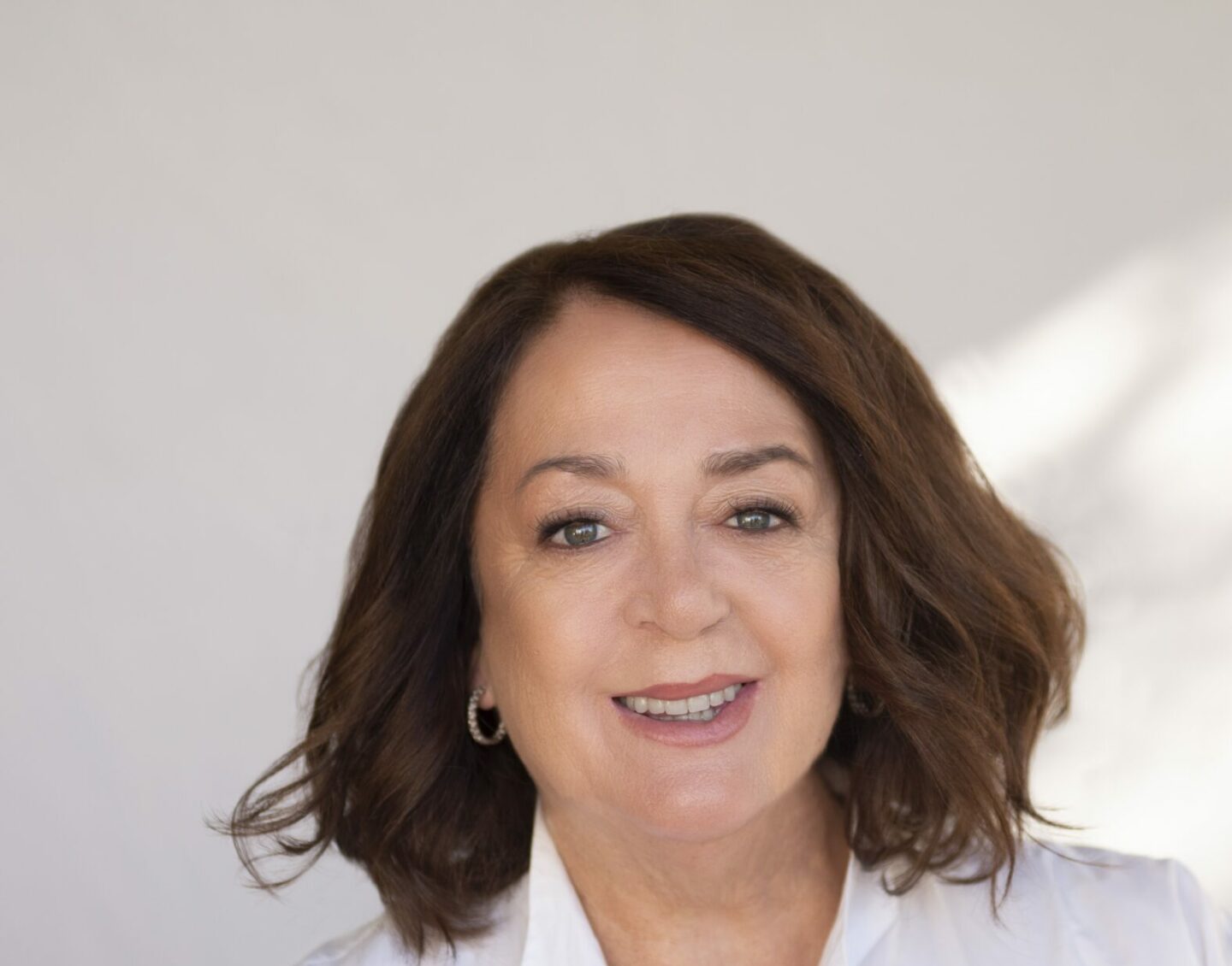 A middle-aged woman with shoulder-length brown hair and a white button up shirt smiles at the camera