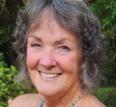 A close up of a smiling woman with chin-length gray air and a beaded necklace