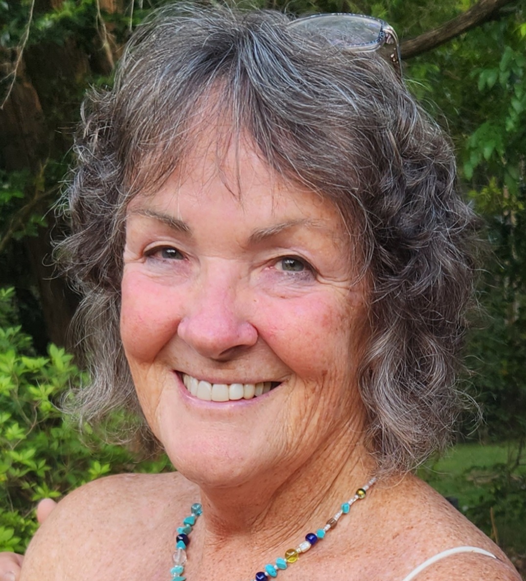 A close up of a smiling woman with chin-length gray air and a beaded necklace