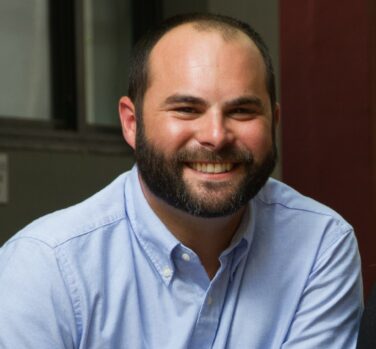 A man with a shaved head and dark beard smiles widely