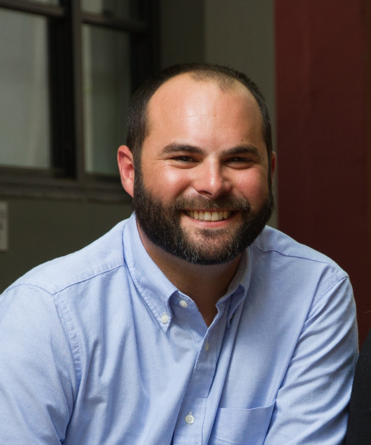 A man with a shaved head and dark beard smiles widely